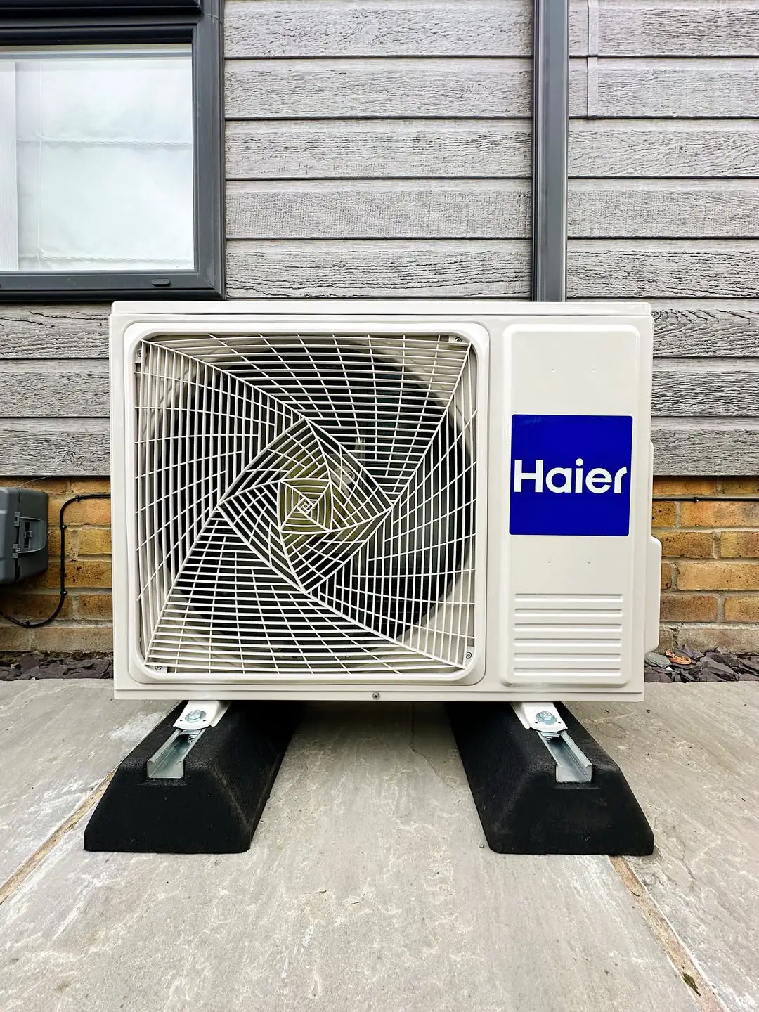 a Haier floor-mounted air conditioning unit providing efficient home cooling and heating, outside a wood panel home, fitted by J. Copland